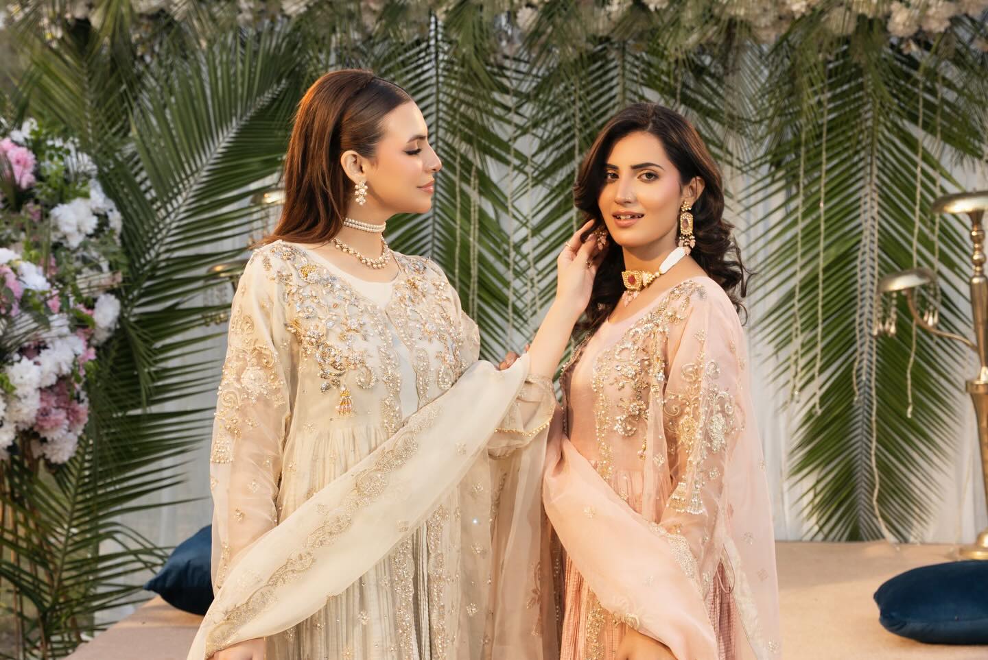Two women in traditional outfits standing next to each other with a decorated background.