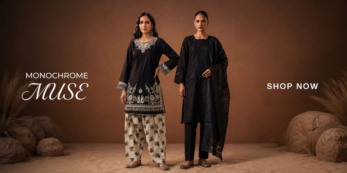 Two women modeling dark monochrome traditional outfits in a styled studio scene with a brown backdrop, decorative rocks, and text reading 'MONOCHROME Muse' and 'SHOP NOW'.